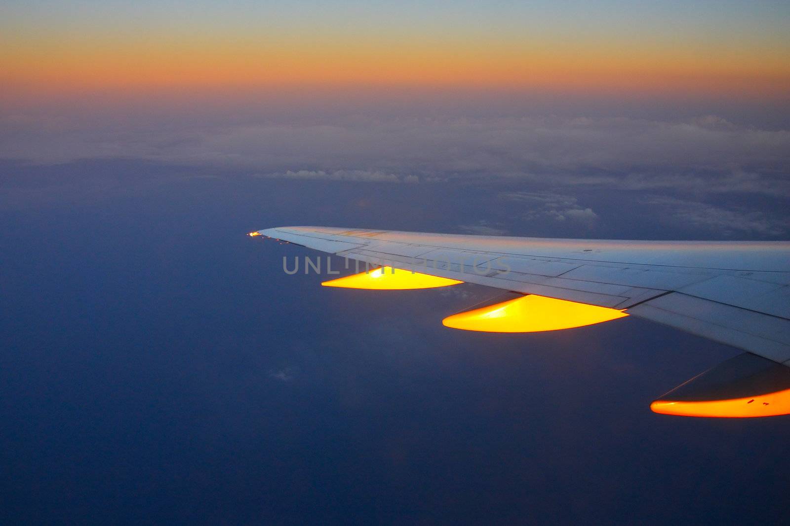 Wing of the plane on a background of gold clouds and sunset