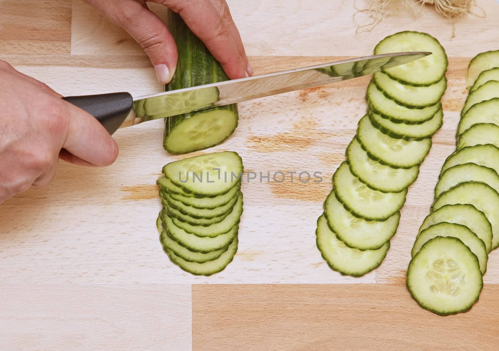 Upper view of hands with a knife chopping a cucumber.