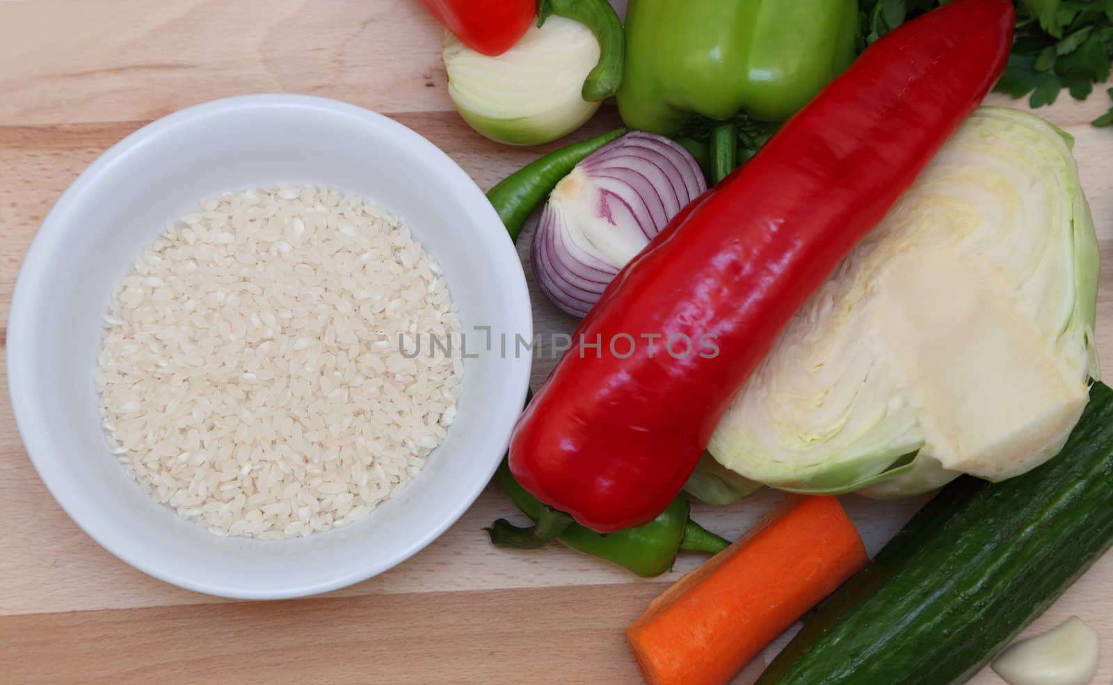 Upper view of a bowl of rice near fresh vegetables on a choping board.