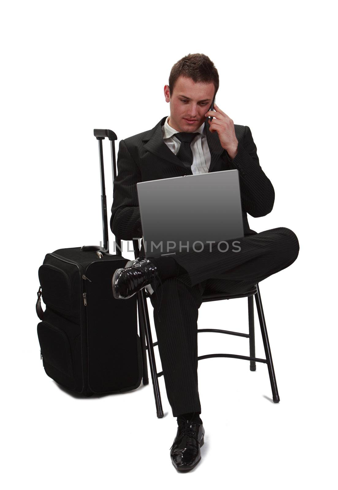 Young and tired traveler businessman working on a laptop while is calling by phone next to his suitcase.