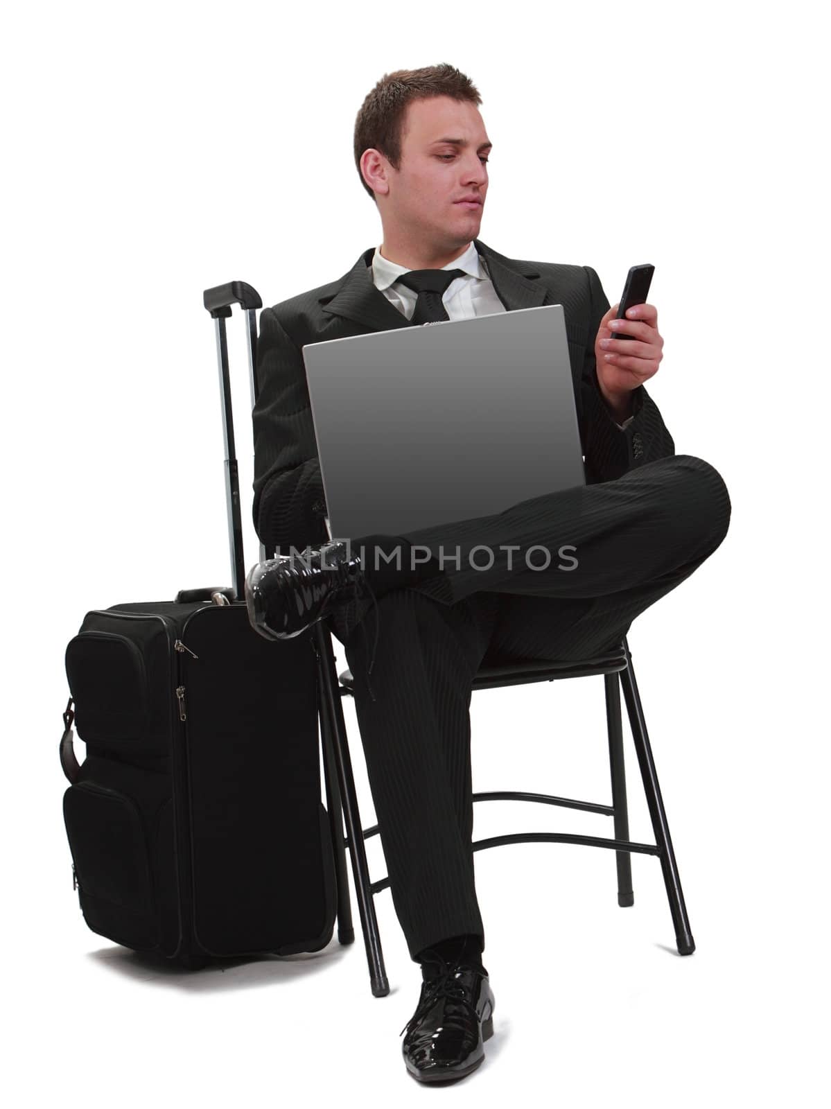 Young businessman reading a phone message while she is sitting with his laptop next to her suitcase,isolated against a white background.