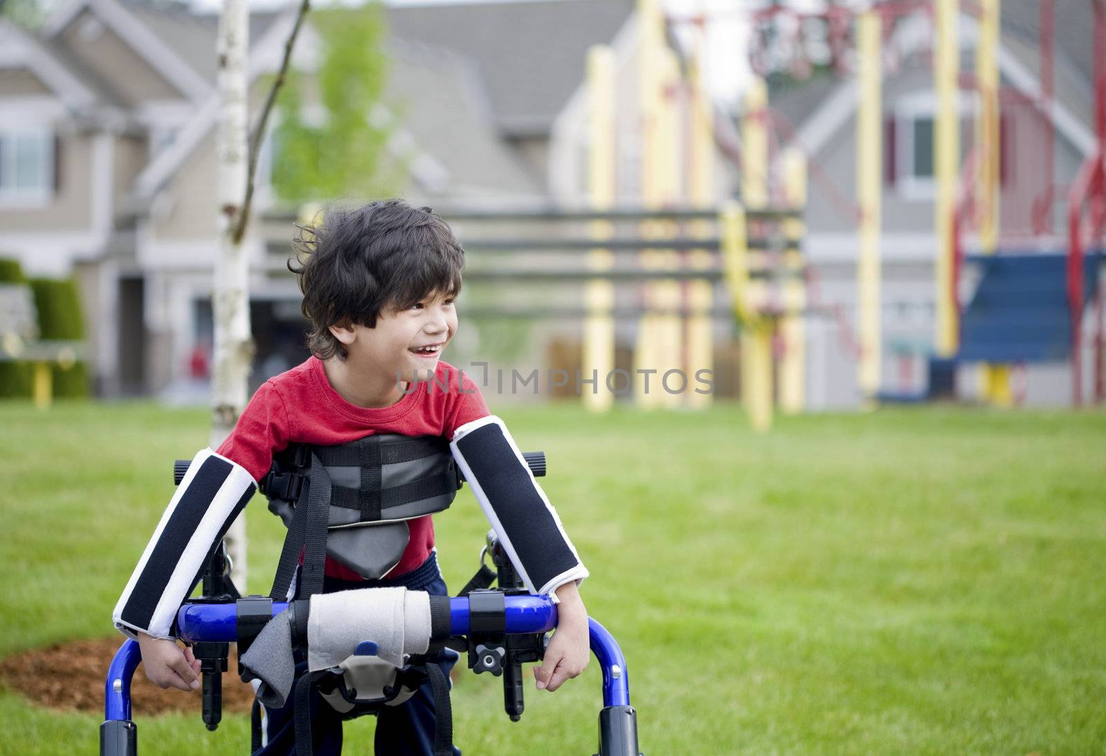 Disabled four year old boy standing in walker near a playground