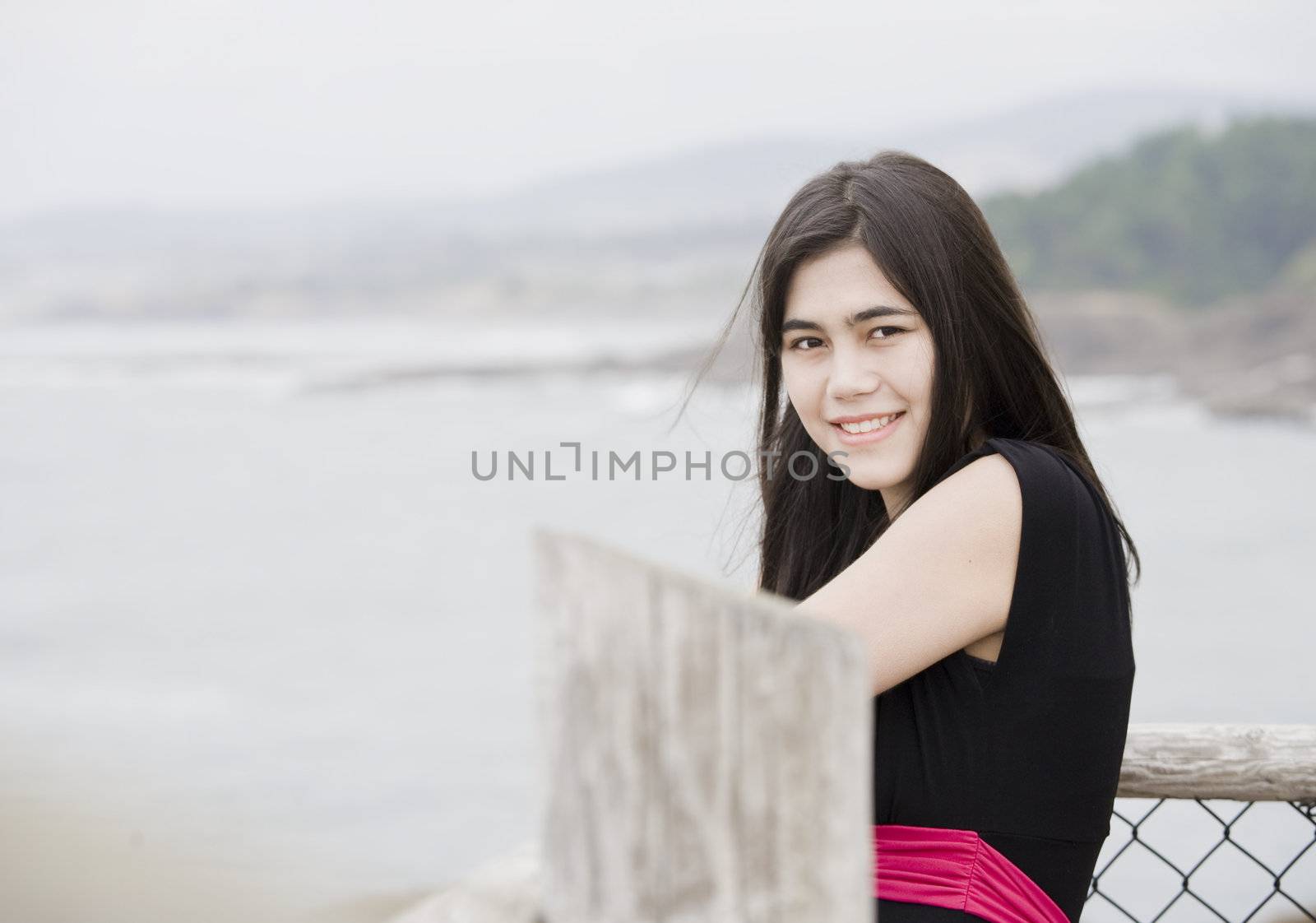 Elegant young woman or teen standing by ocean in simple black dress