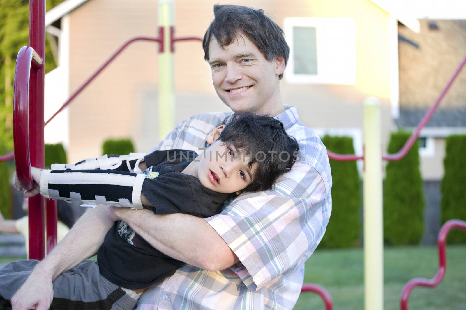 Father helping disabled son to play at playground by jarenwicklund