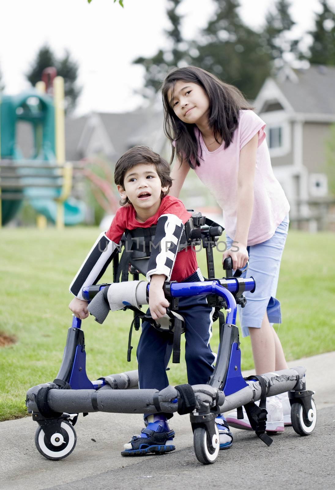 Big sister helping younger disabled brother in walker by jarenwicklund