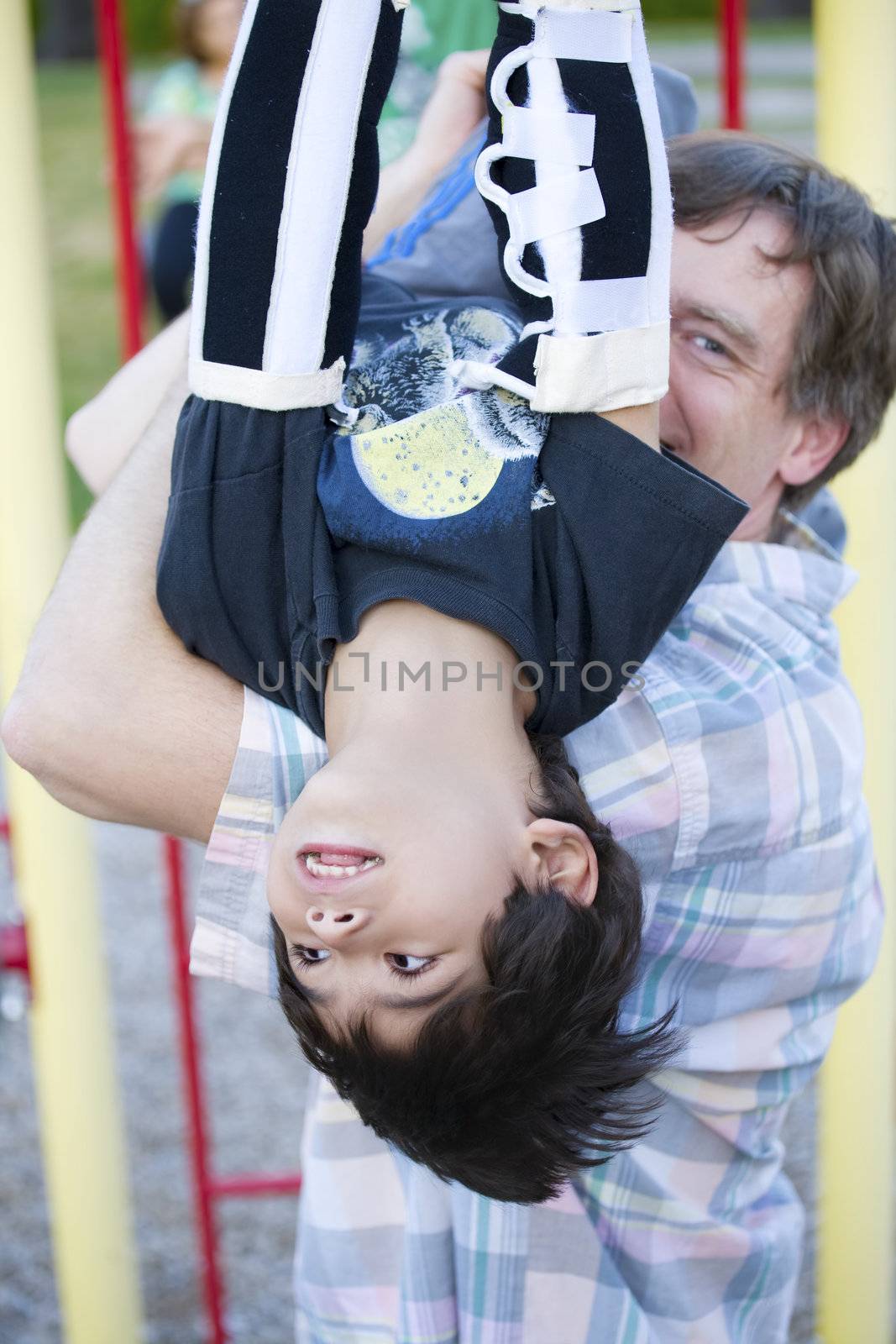 Active disabled five year old boy playing on the  monkey bars with his father