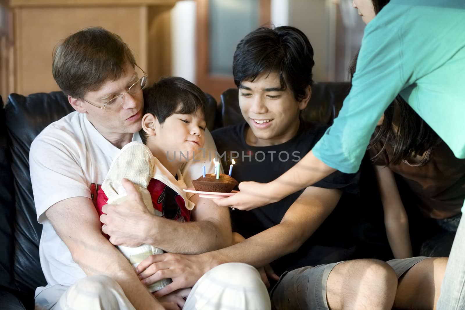 Disabled five year old boy blowing out birthday candles with family