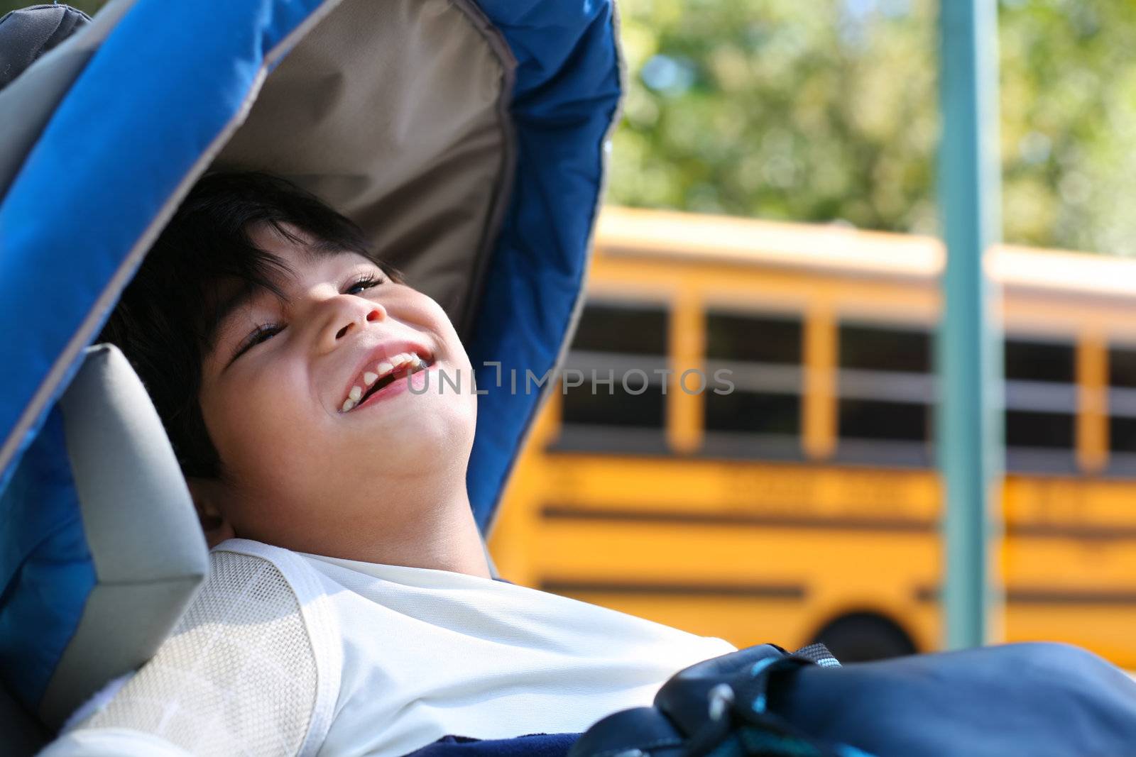 Disabled five year old boy in wheelchair outdoors by school bus