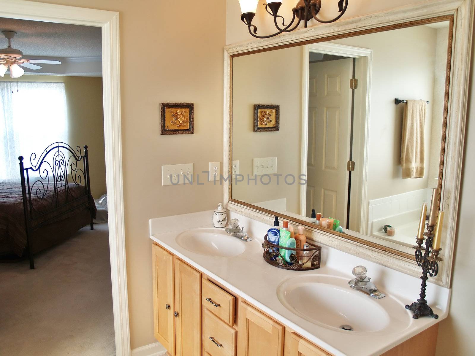 A modern luxurious bathroom with a large in an American home. A bed is visible through the doorway in the background.