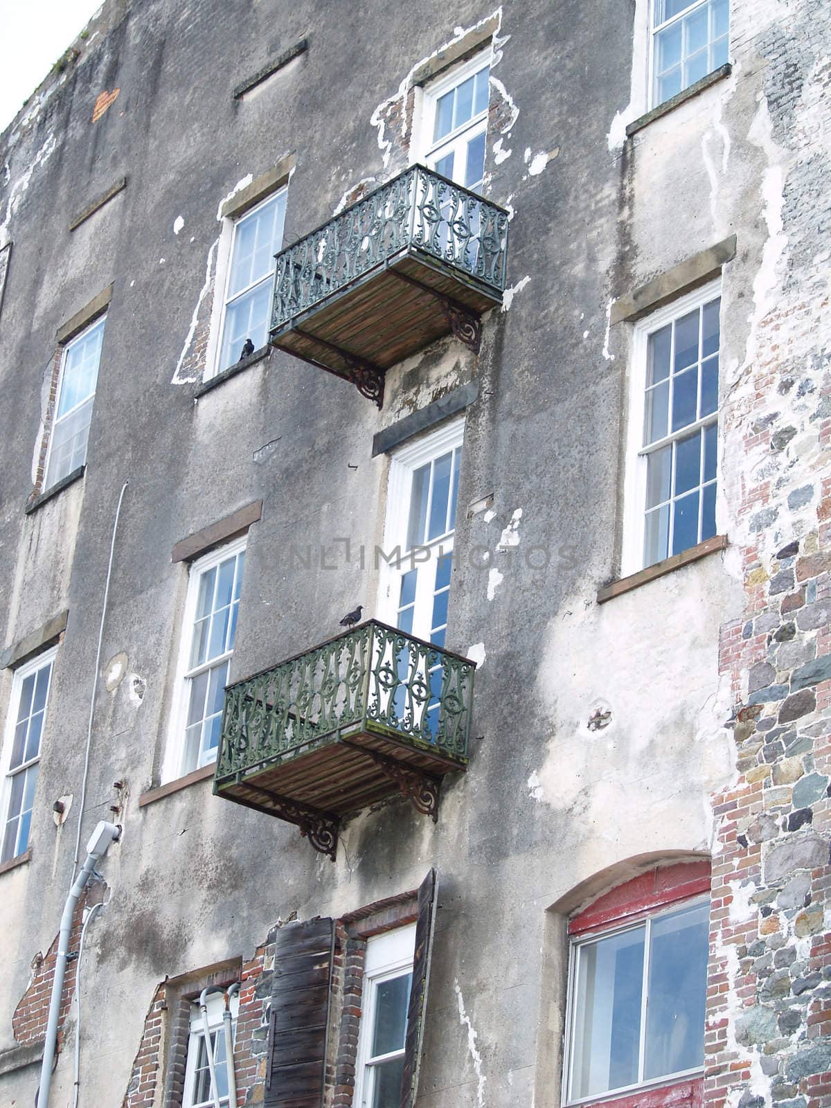 Wrought iron balconies attached to an old waterfront multistory building. The blue sky is reflected in the white wooden windows.
