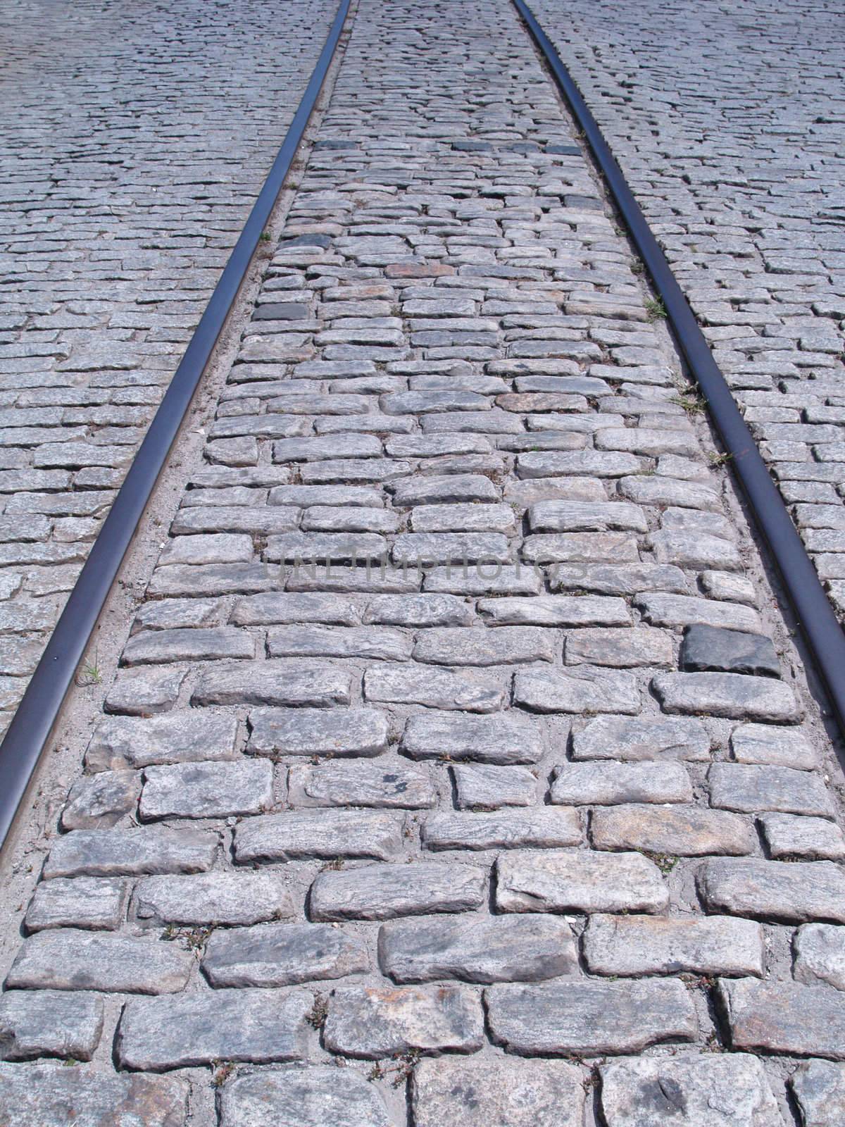 Train tracks embedded in down the middle of an old cobblestone road.