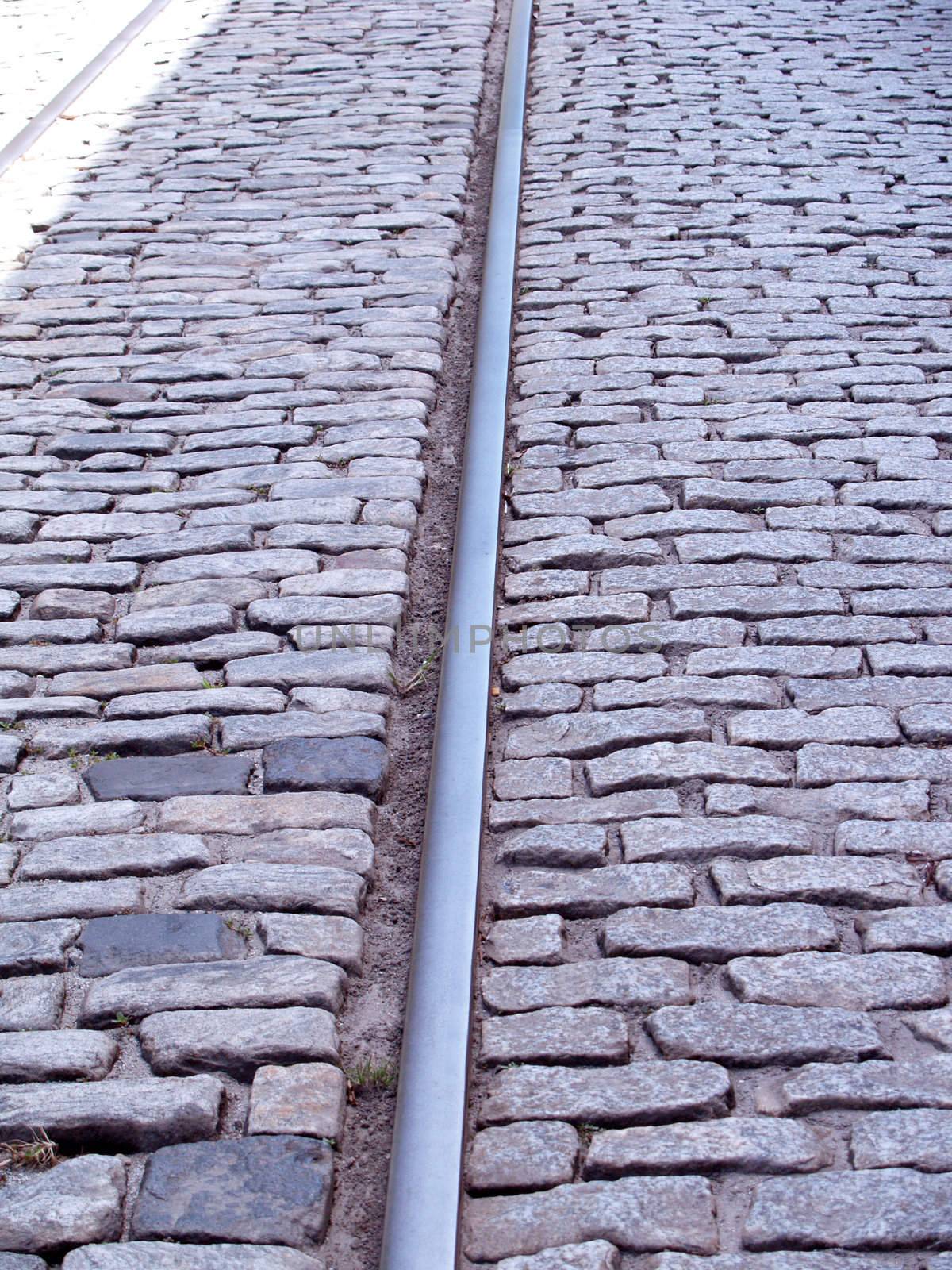 Closeup view of train tracks embedded in down the middle of an old cobblestone road.      