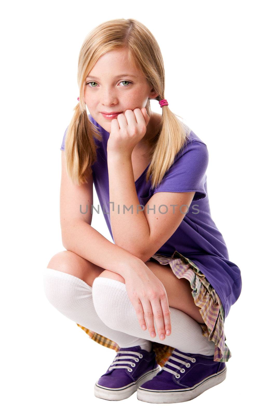 Beautiful happy teenage girl sitting squatted wearing knee socks, puple sporty shoes, shirt and colorful skirt, hand supporting her head, isolated. 