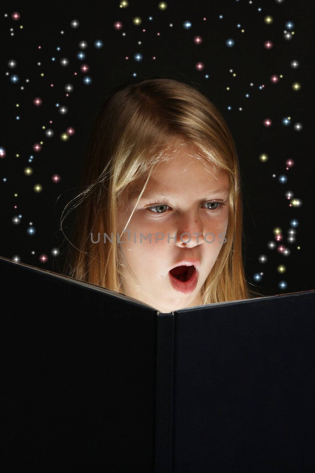 Pretty young school girl engrossed in reading a book with stars coming out of it