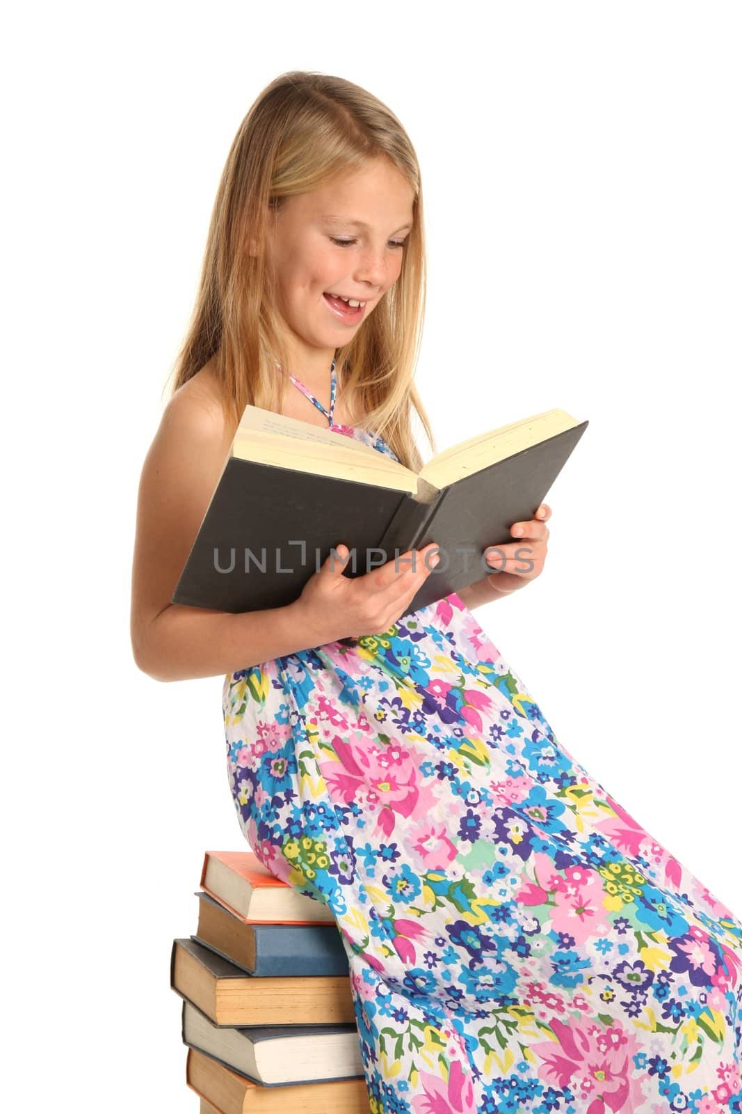 Beautiful young school girl sitting on a pile of books and reading