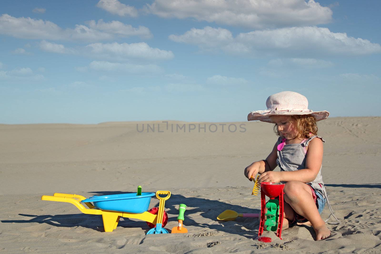 little girl play with toys in sand by goce