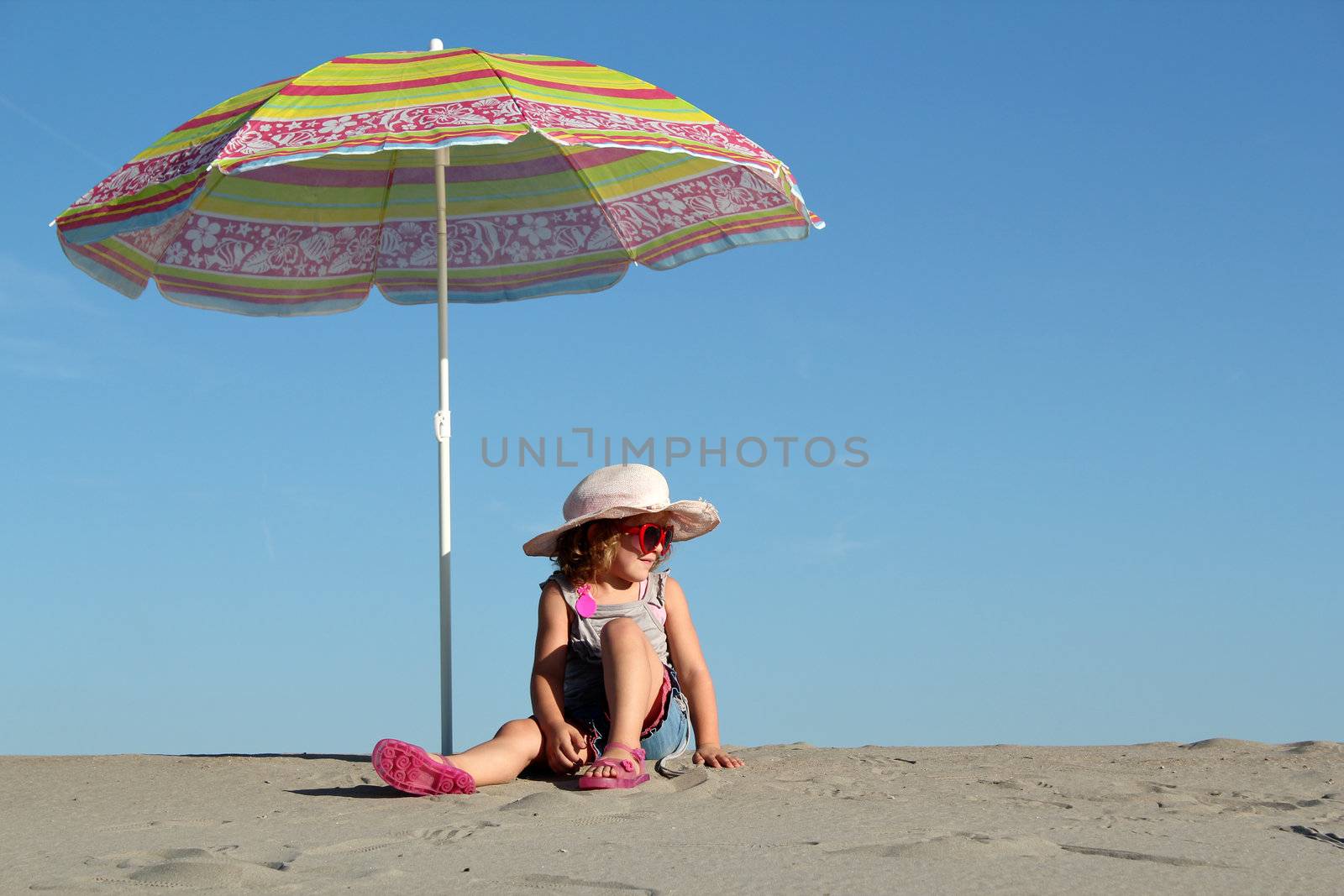little girl with sunglasses sitting under sunshade by goce