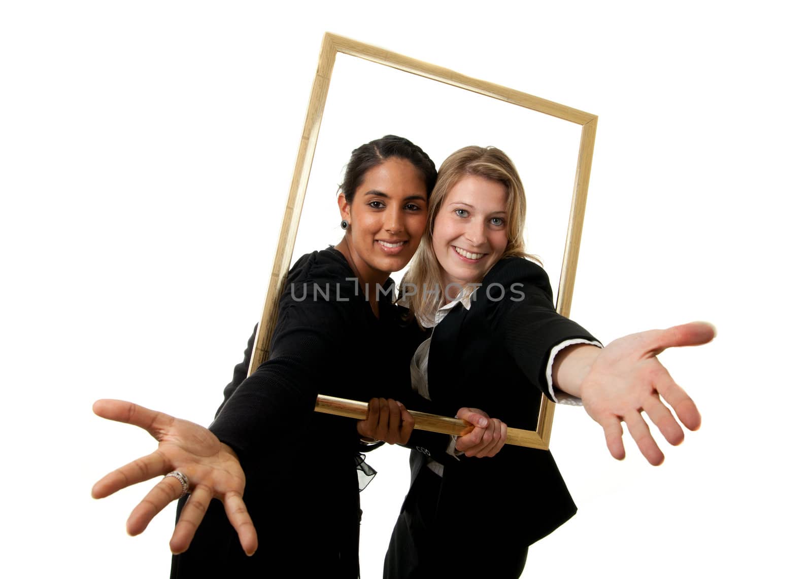 a young indian and a young european businesswoman stretching their hands through a pictureframe