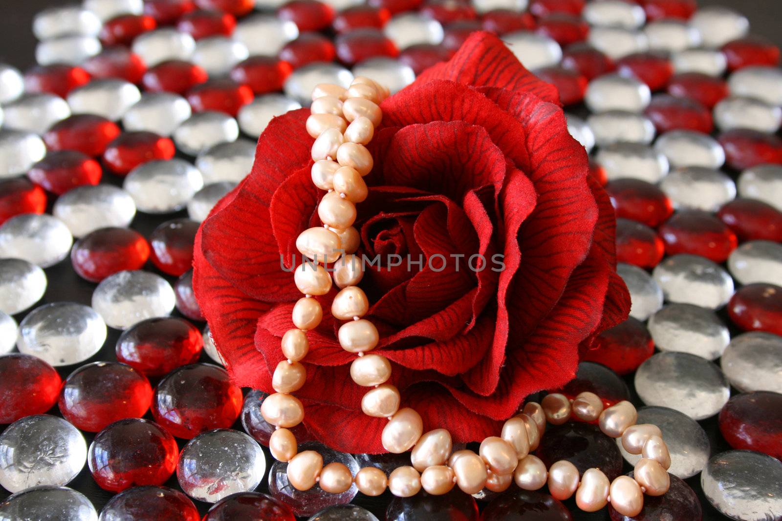 Artificial rose with real pearls on a surface of glass pebbles