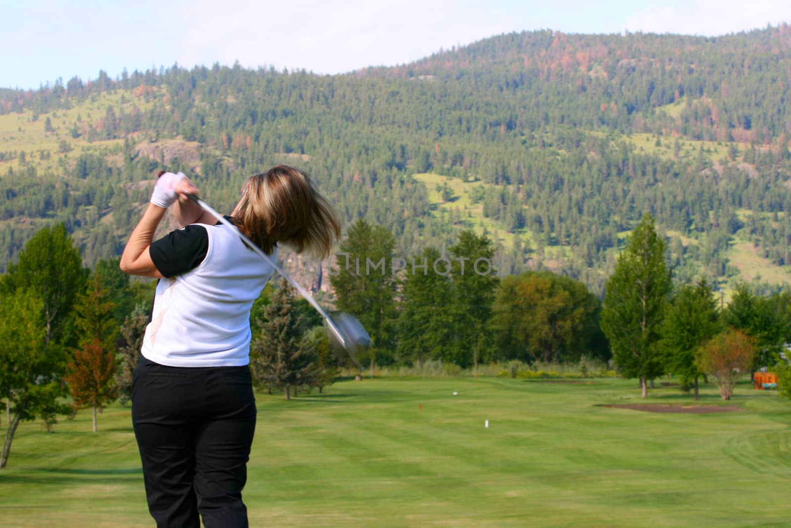 Blond female golfer following her shot from the tee-box down the fairway 