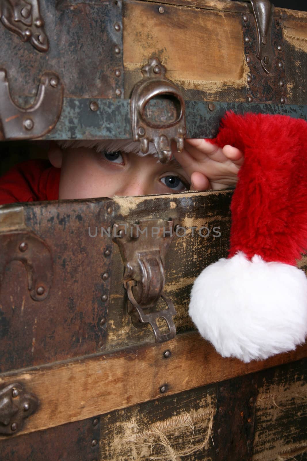 Serious boy with a christmas hat peeping from inside an antique trunk