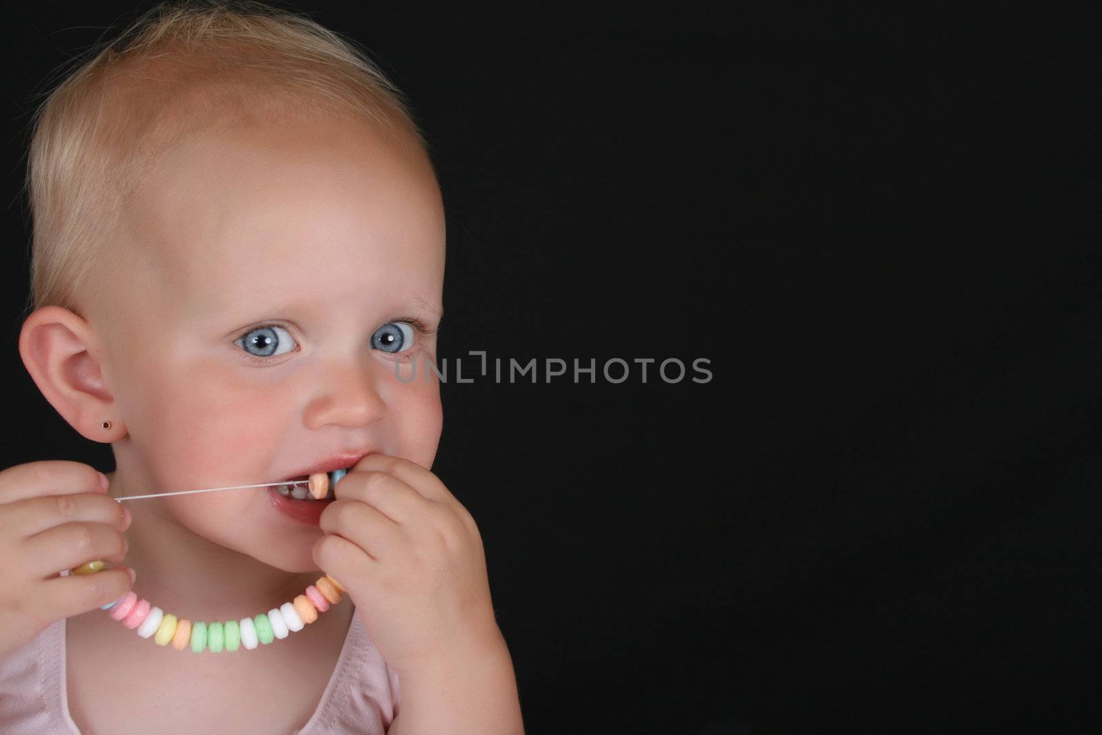 Cute blond toddler eating a candy necklace