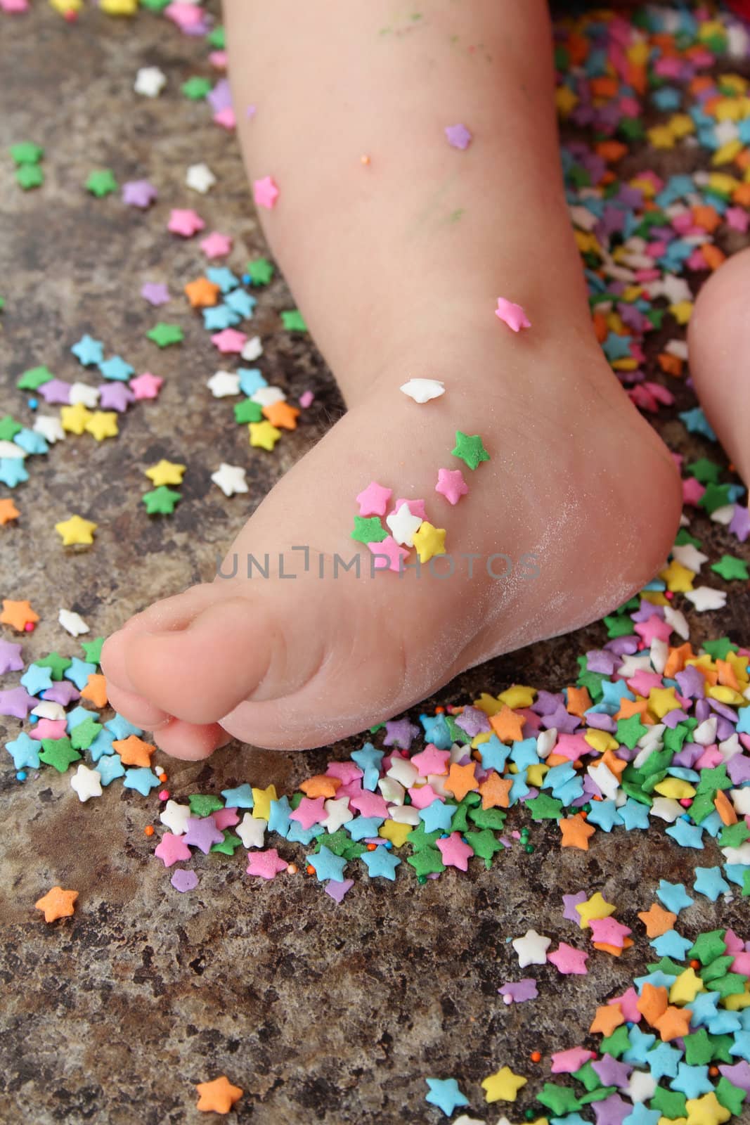 Baby foot on kitchen countertop surrounded with cake decorations