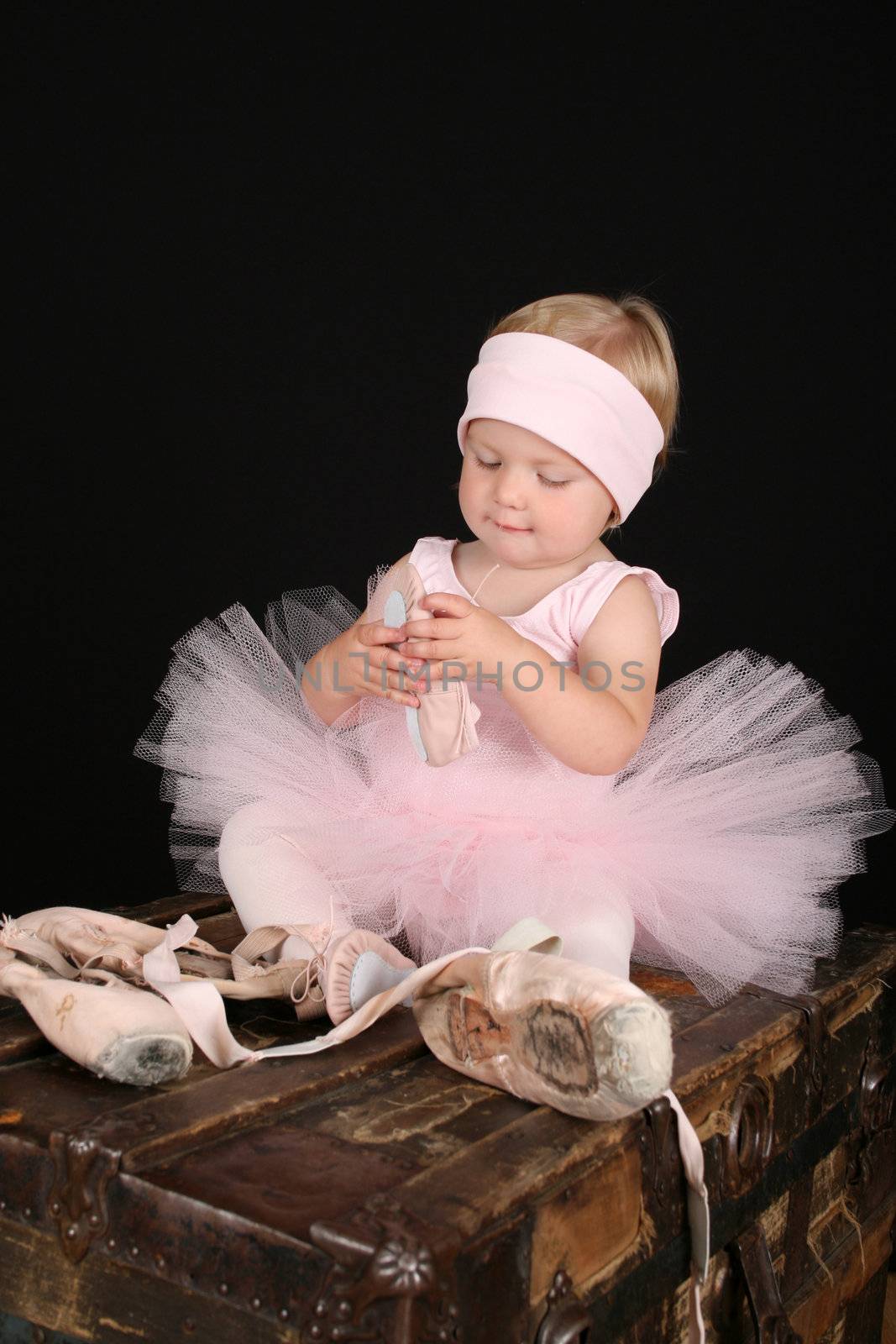 Blond toddler wearing a tutu holding Ballet shoes 