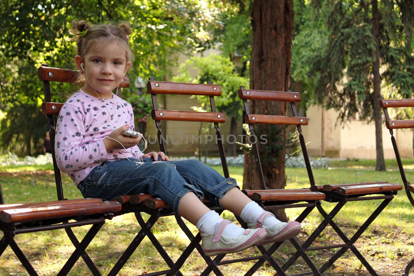 little girl sitting in the  park and listen music on phone by goce