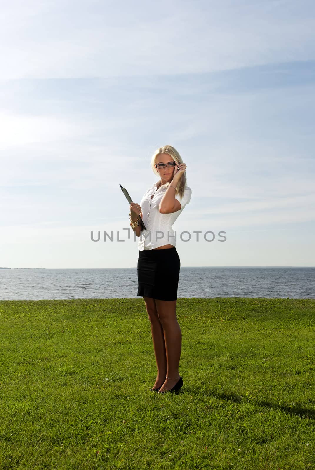 girl in glasses standing with a folder on the background of the sea, sky and grass