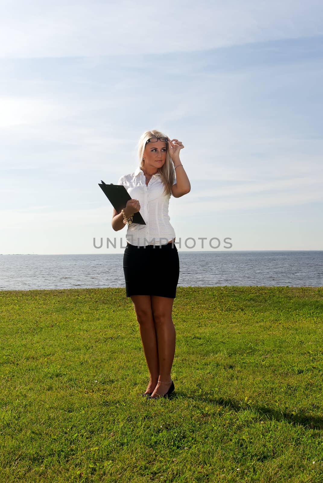 girl in glasses standing with a folder on the background of the sea, sky and grass