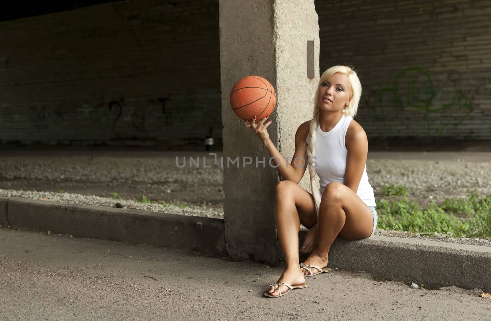 Beautiful blonde girl is sitting with basketball on the street