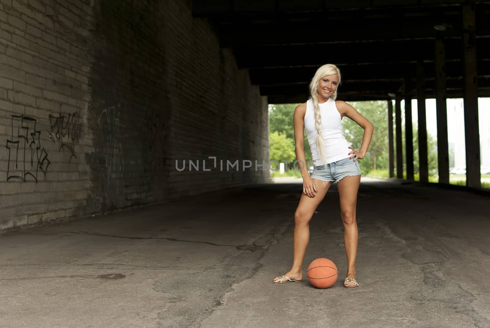 Beautiful blonde girl standing with basketball in the street