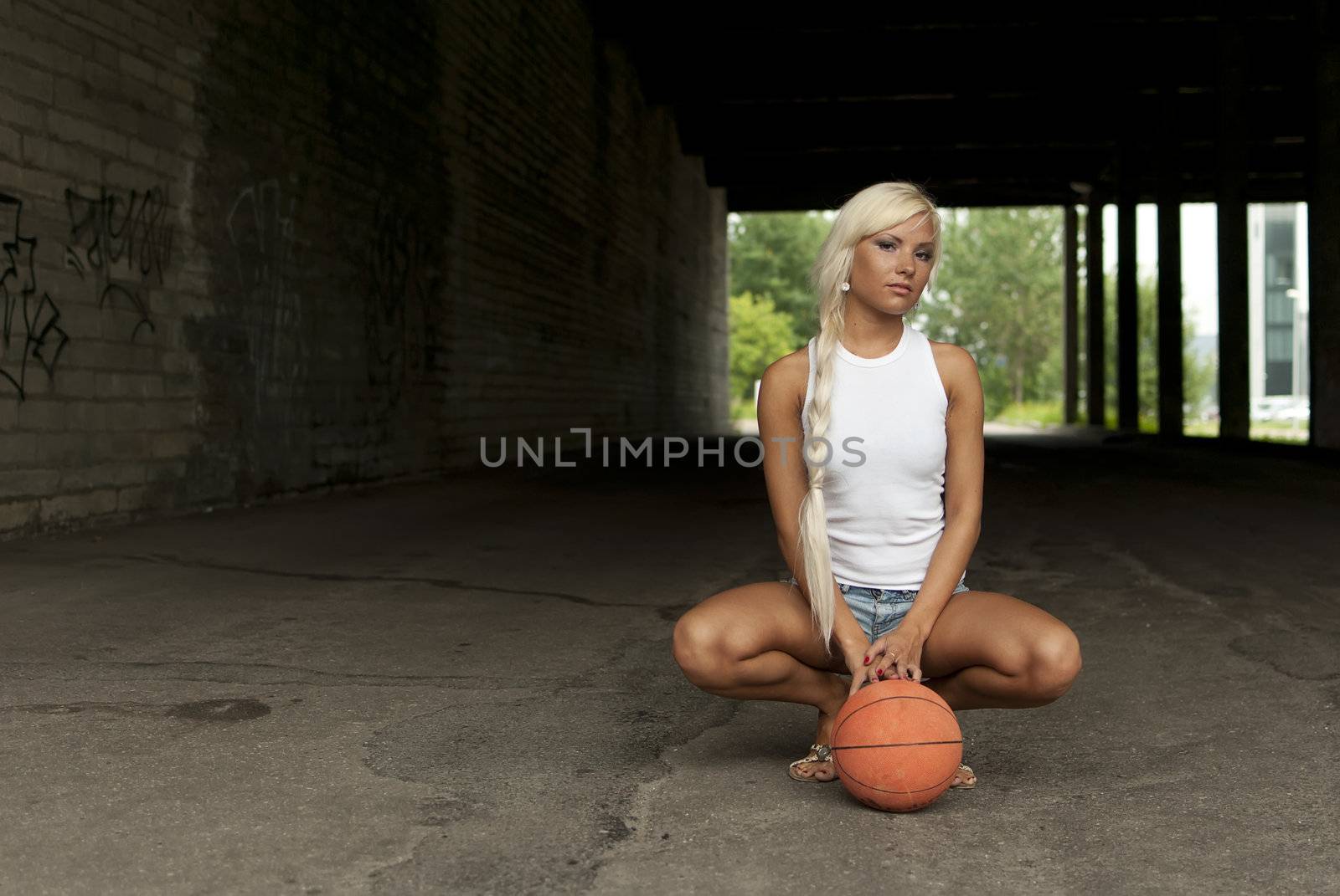 Beautiful blonde girl is sitting with basketball on the street