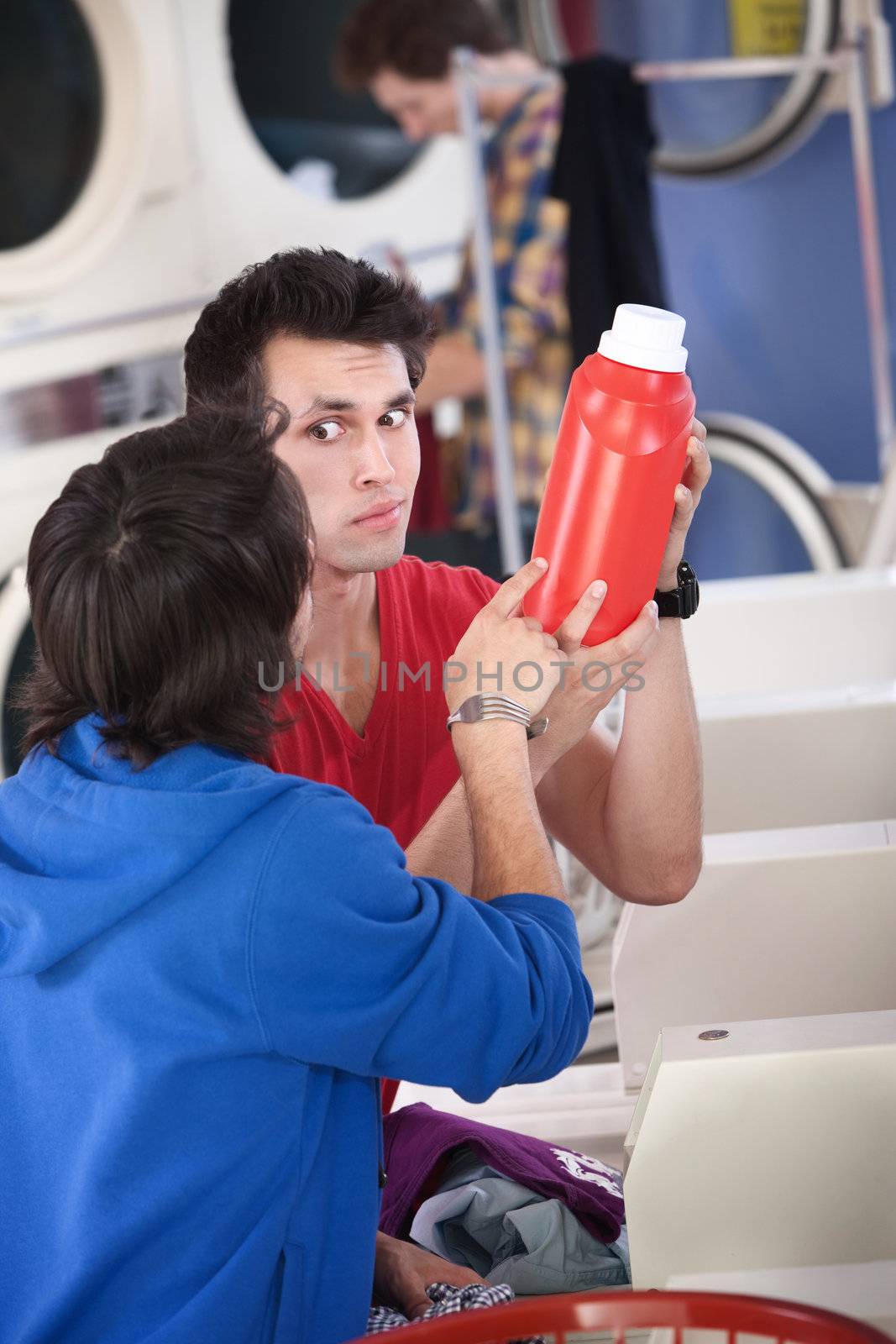 Two confused young men in laundromat read the instructions on detergent or conditioner canister