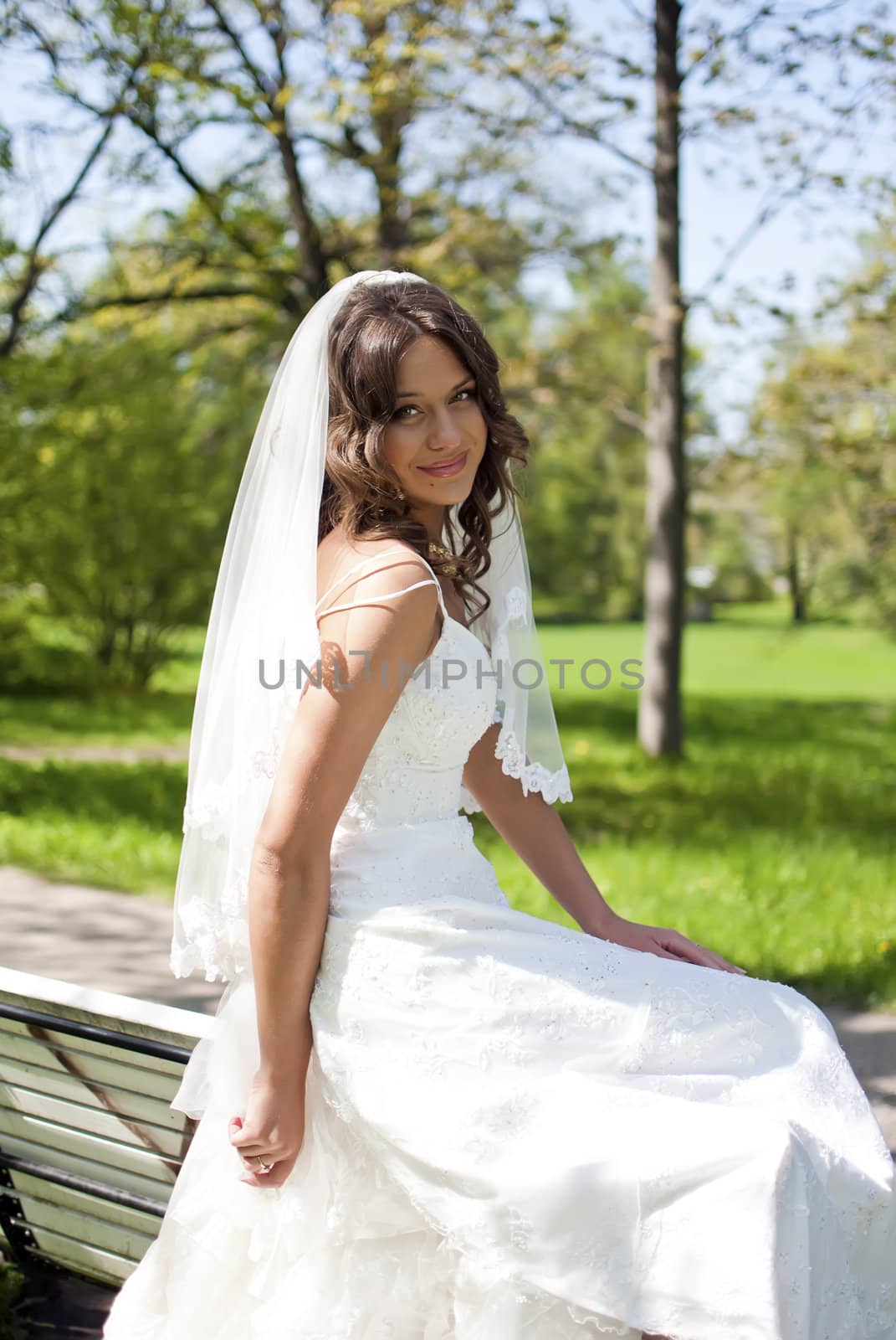 beautiful young bride sitting on a park bench