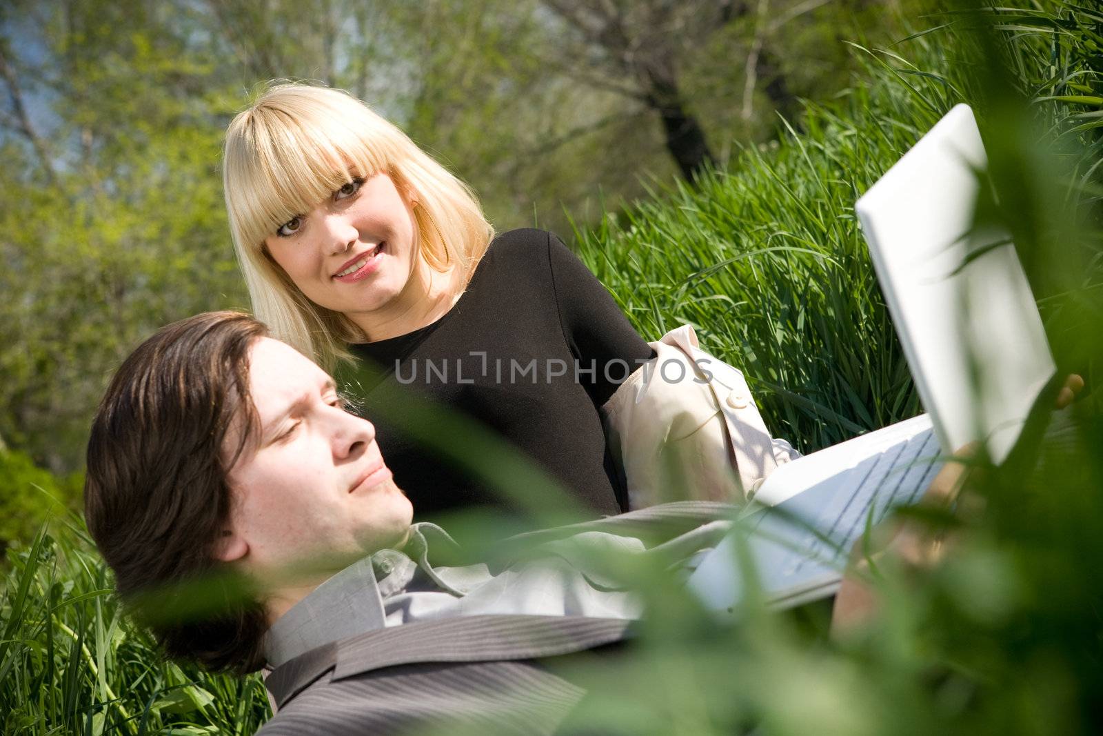 a couple working on laptop in nature on the grass field by vsurkov