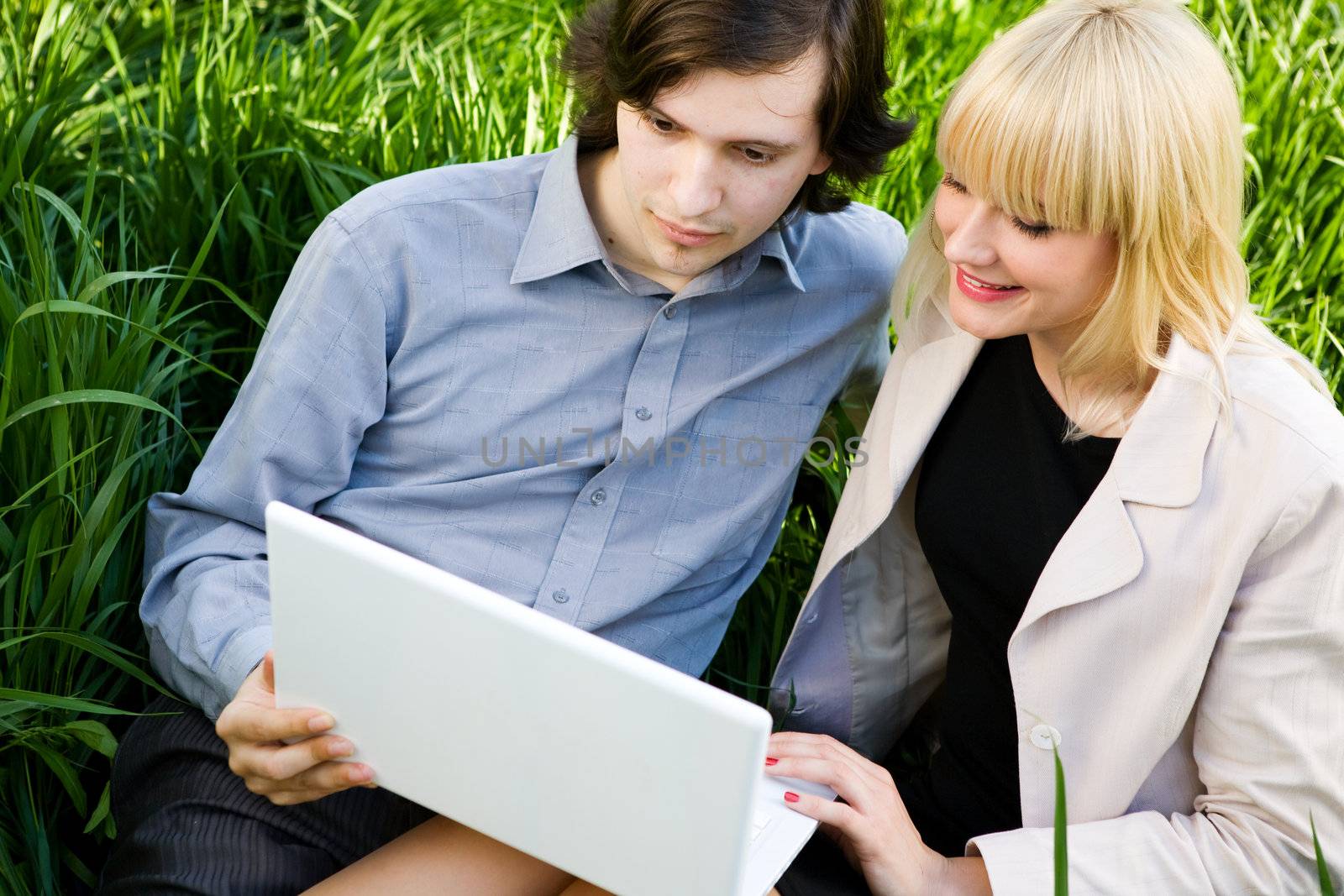 boy and girl sit on the grass and look in laptop