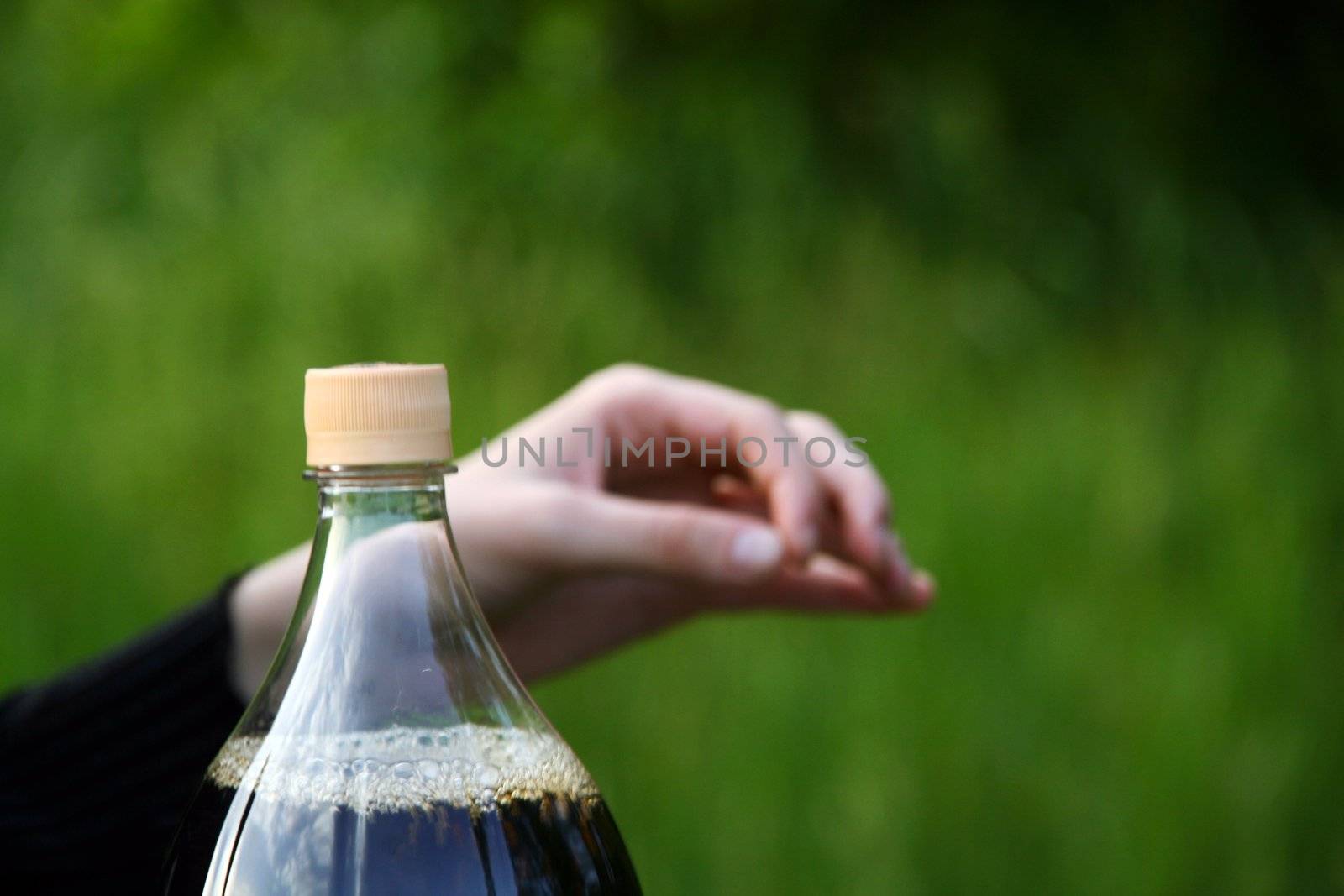 Human hand and bottle of Coca-Cola on green backgroud