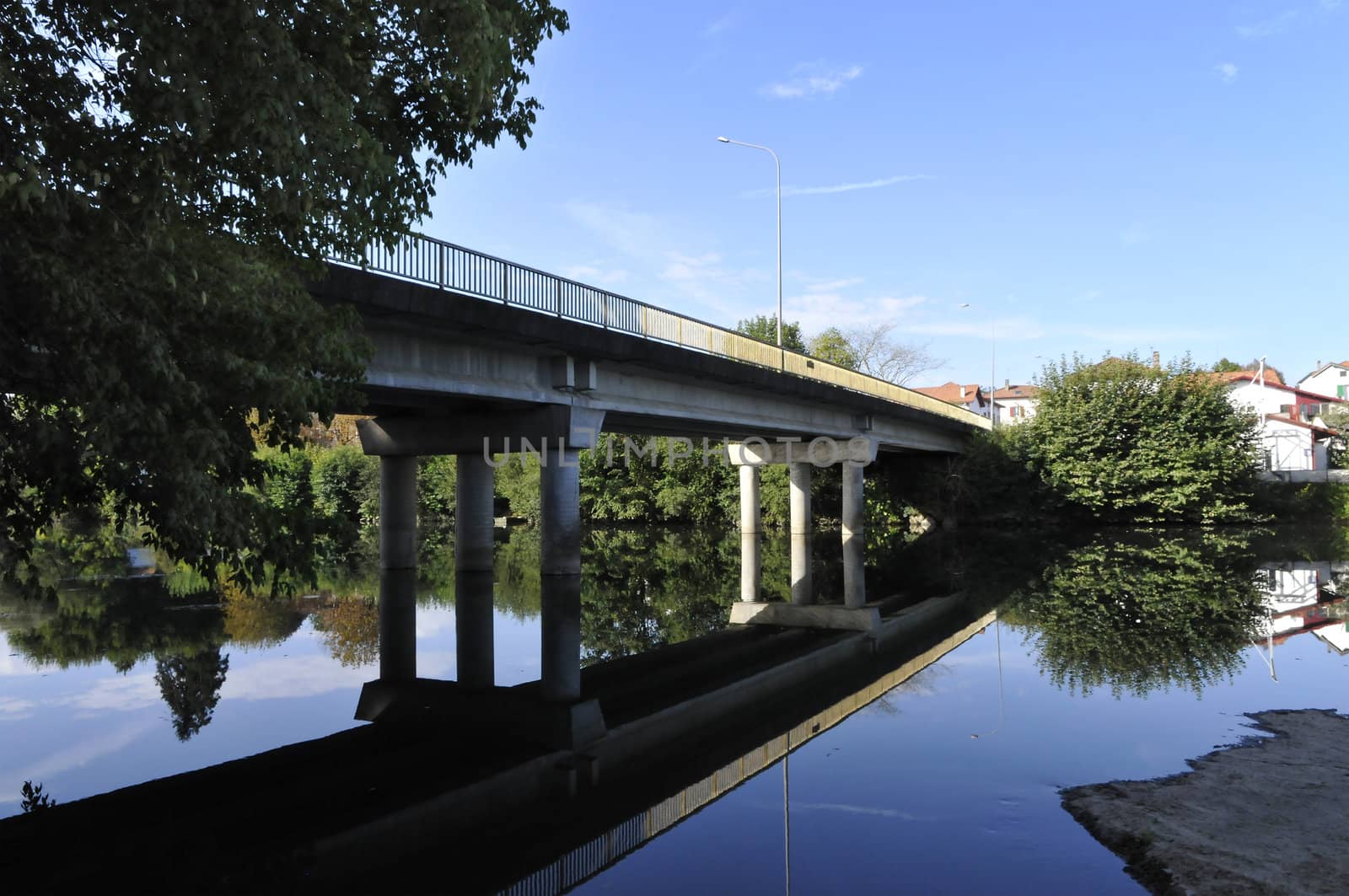 Modern concrete bridge across a river with its reflection and a blue sky