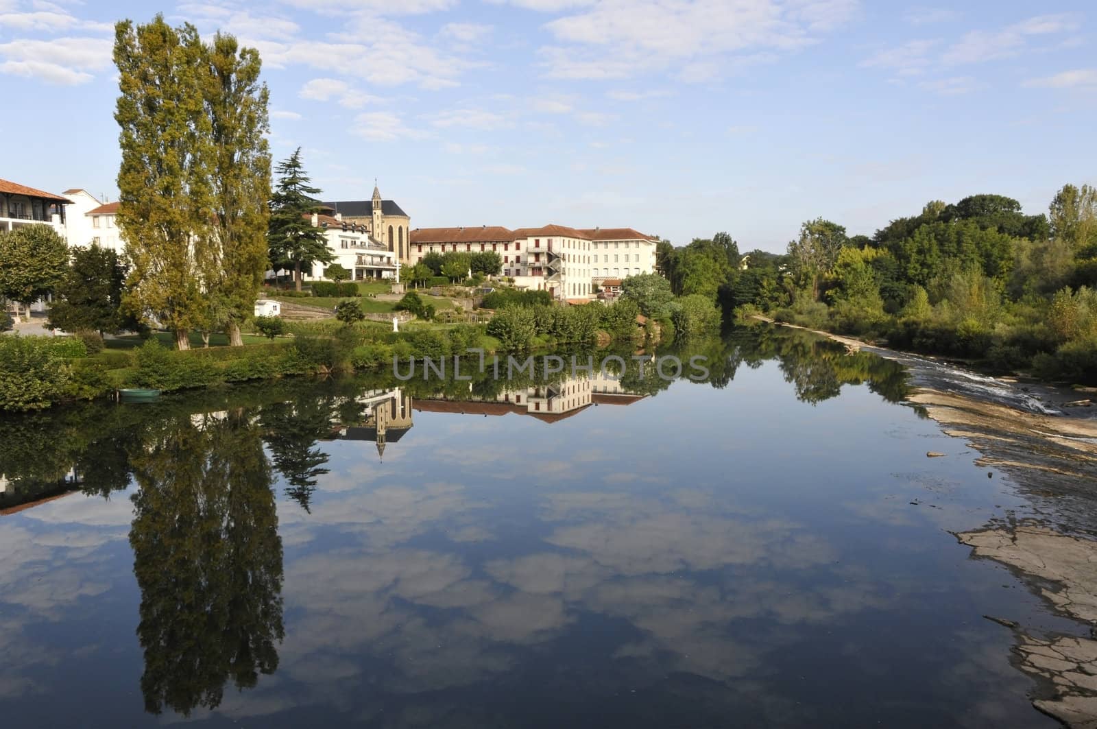 Sky reflection on a river with trees and some little buildings