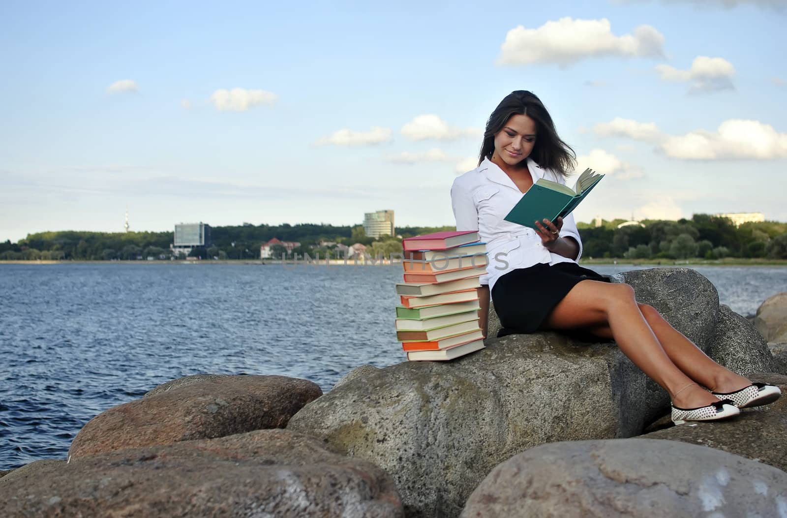 girl with books sitting on a rock by the sea