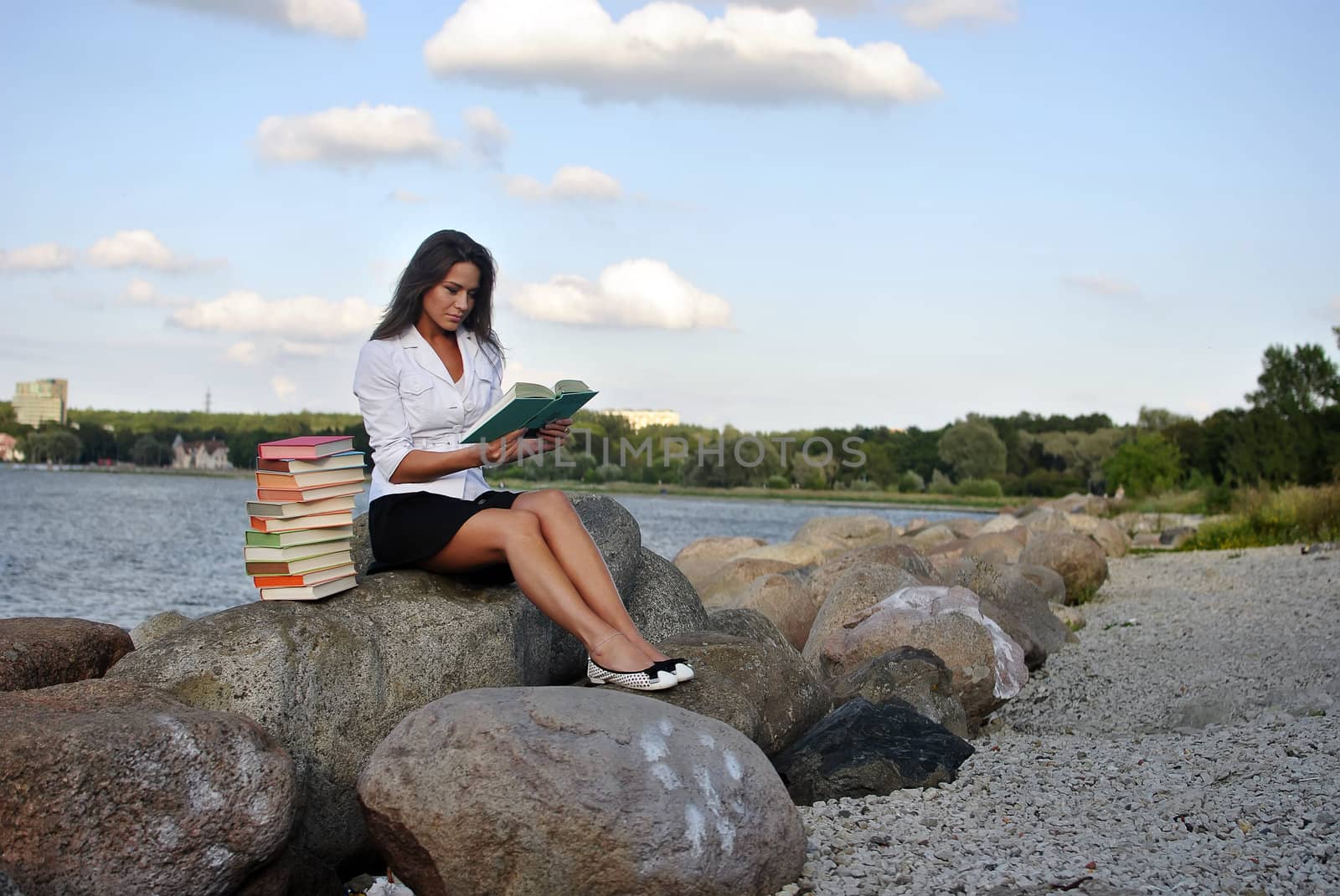 girl with books sitting on a rock by the sea