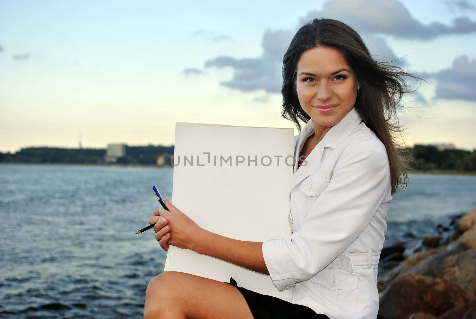 beautiful girl in a white jacket holding blank paper. sea on the background