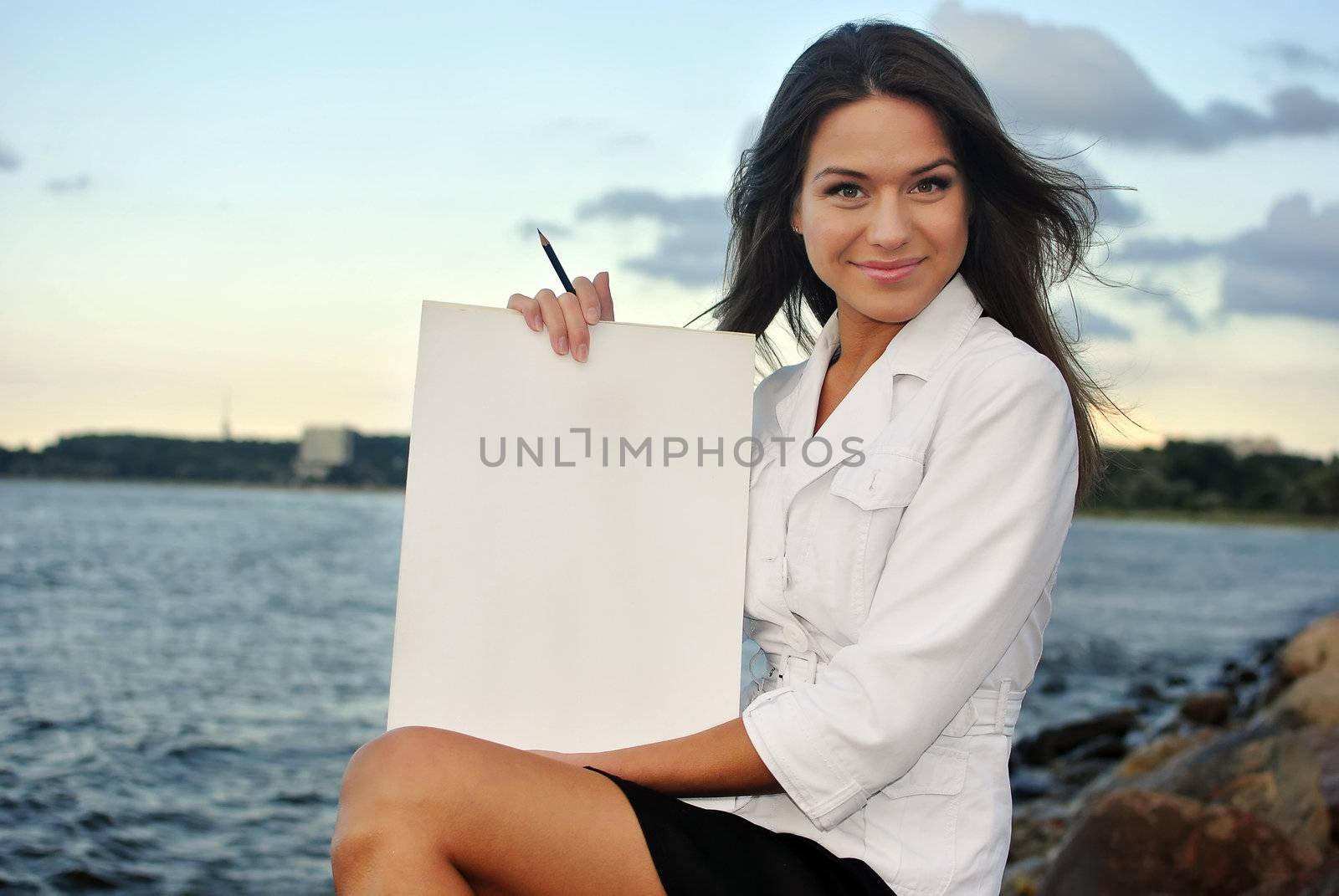 beautiful girl in a white jacket holding blank paper. sea on the background