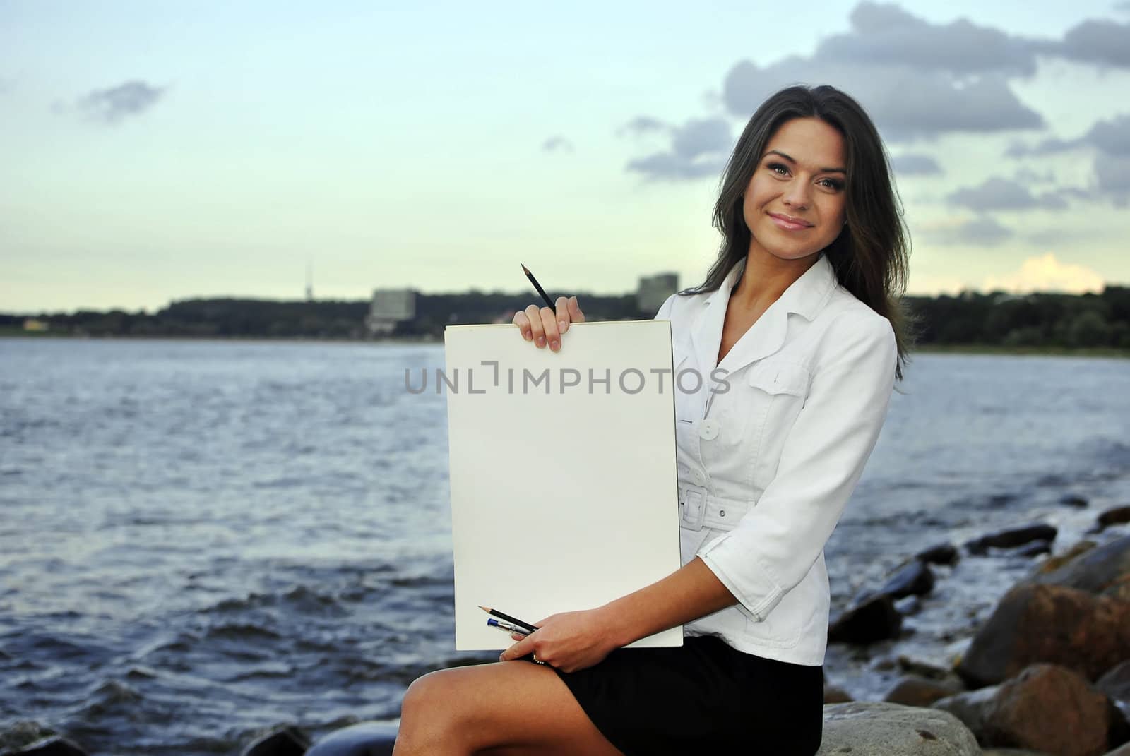 beautiful girl in a white jacket holding blank paper. sea on the background