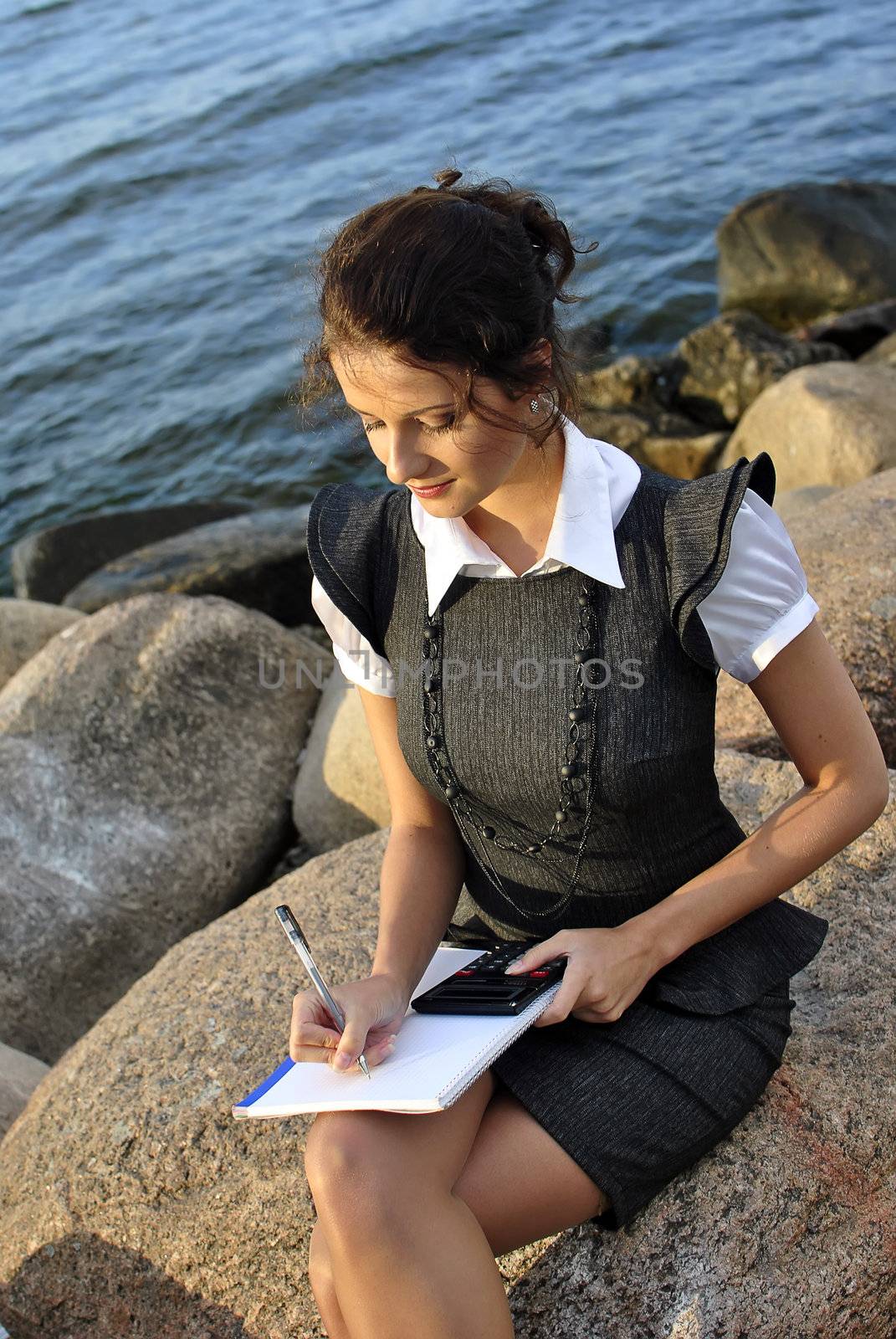 beautiful girl with a notebook and a calculator sitting on the rocks