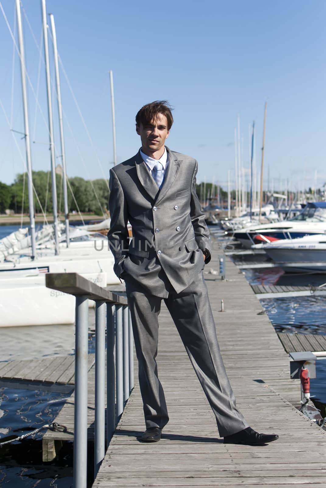 man in a gray suit, standing on the beach near the yacht