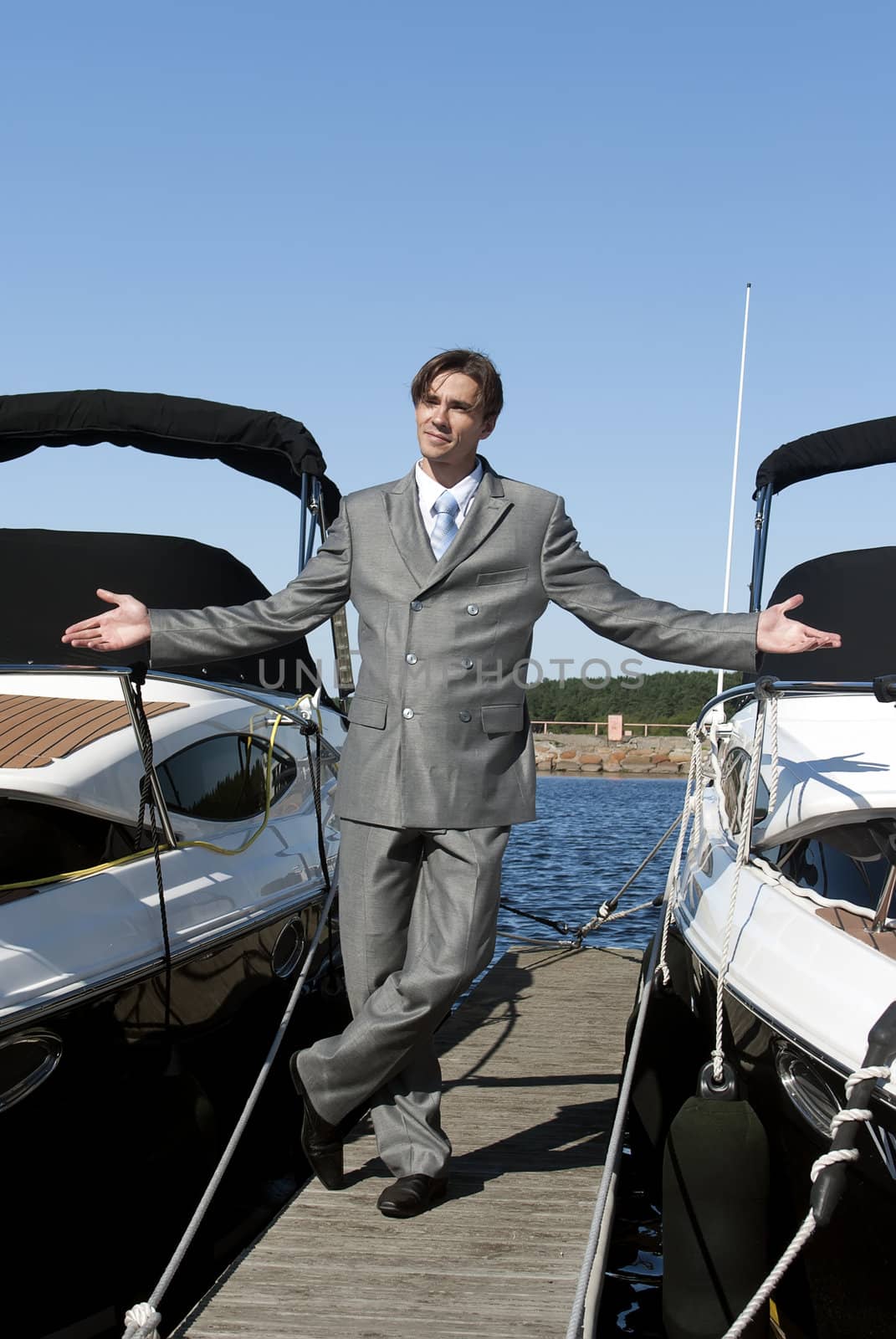 man in a gray suit, standing on the beach near the yacht