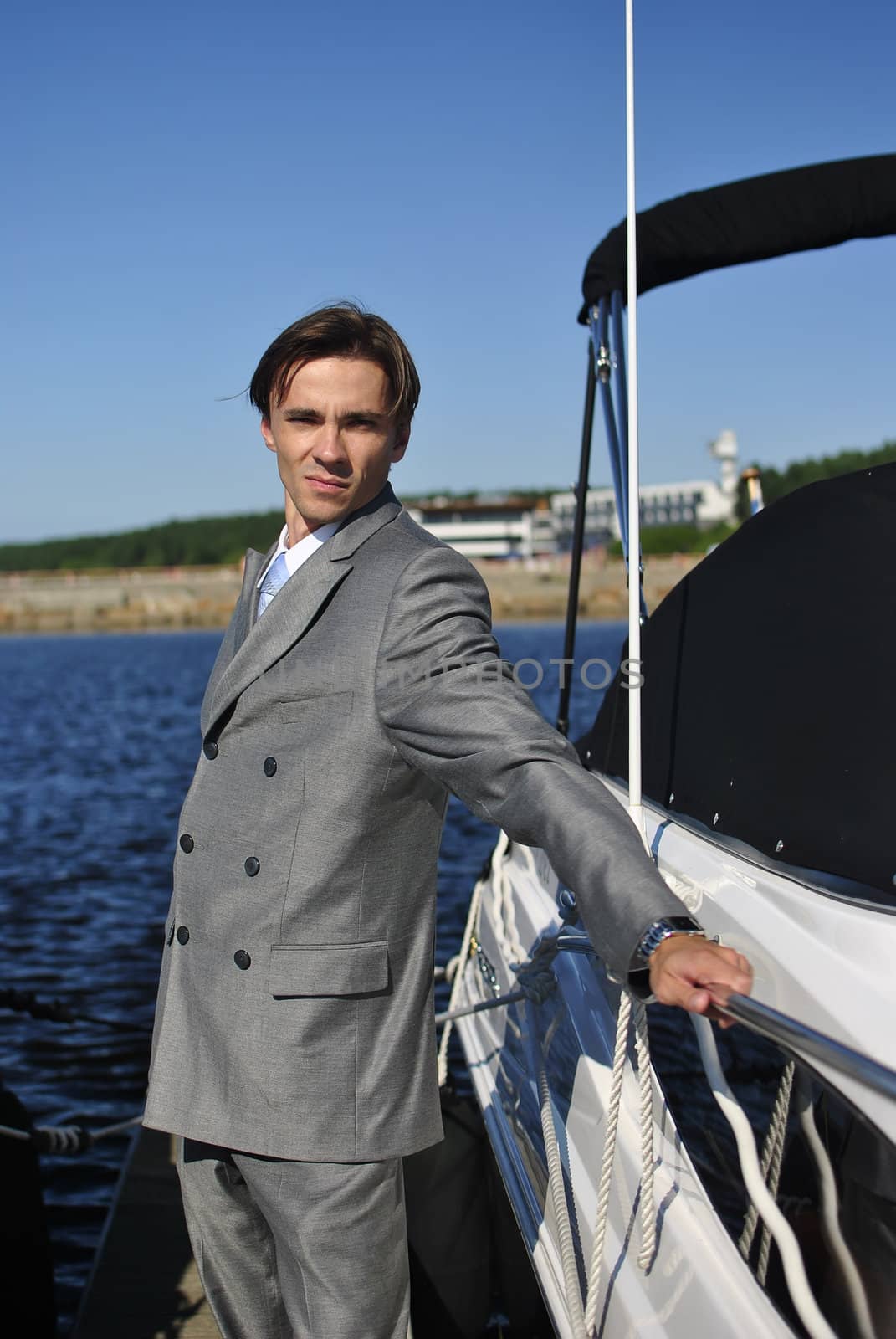 man in a gray suit, standing on the beach near the yacht